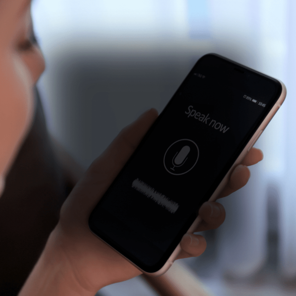 A person holding a cellphone with speak now on the screen above a microphone icon.